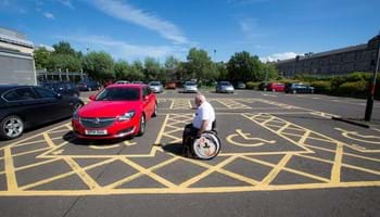 A wheel chair user wheels past disabled parking bays.