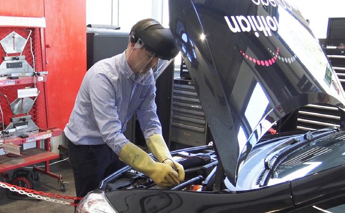 Someone wearing a protective helmet and gloves working in the bonnet of an electric car.