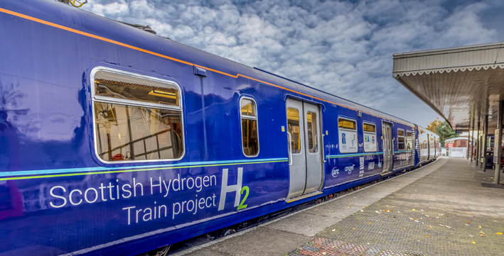 The side of a blue hydrogen train in the station. It has Scottish Hydrogen Train Project written on the side.