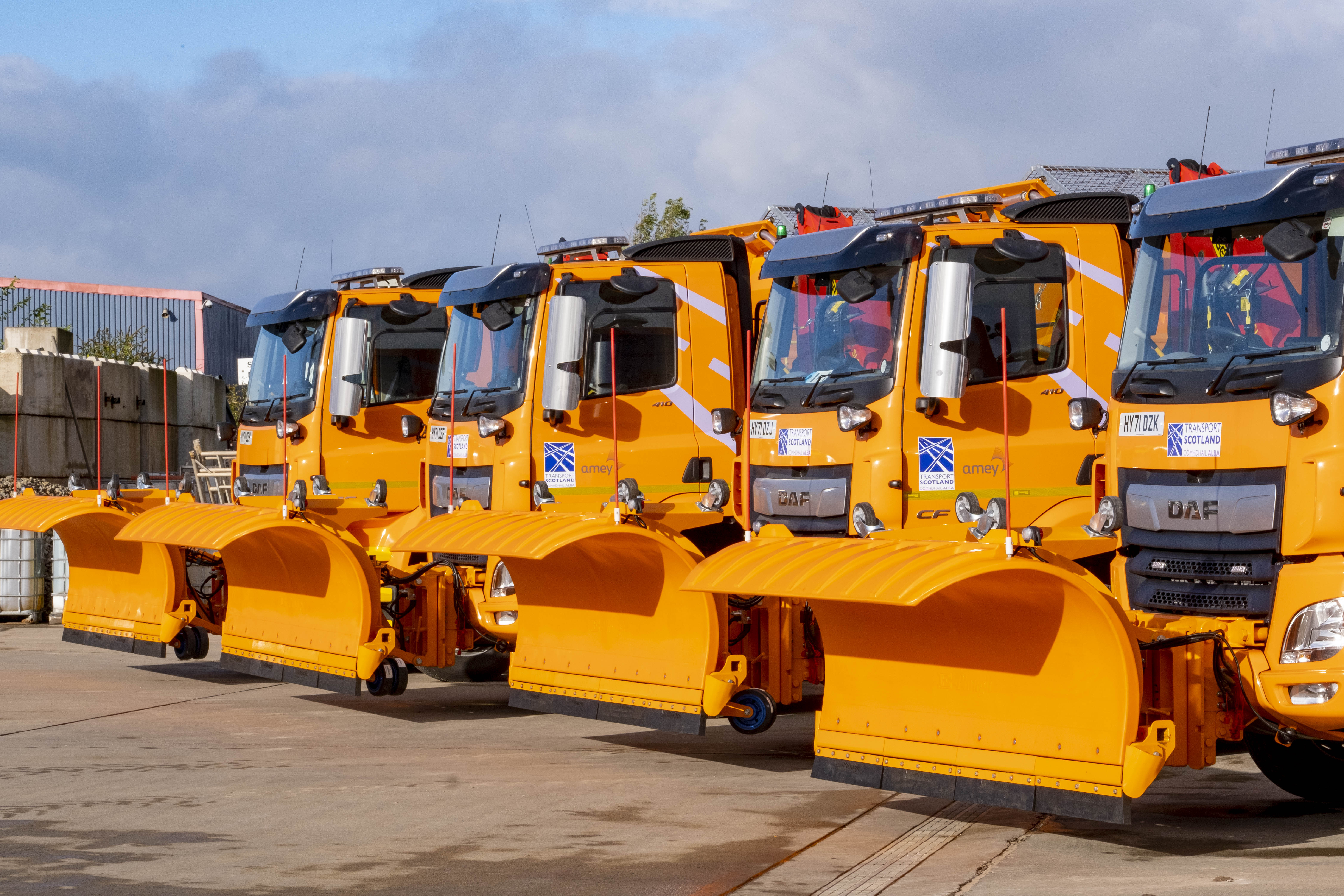 Four gritters lined up outside at a depot.
