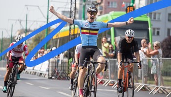 A cyclist celebrates winning a road bike event. As he rides, he spreads his arms and cheers.