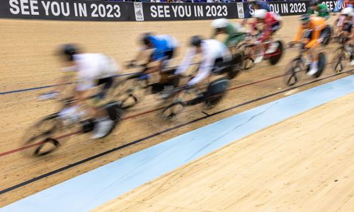 A group of cyclists race around a velodrome track at speed.