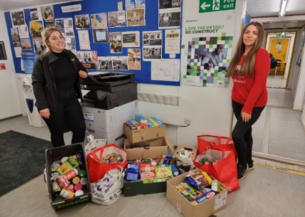 Photograph of two Farrans staff members standing in their office with bags of food to be donated