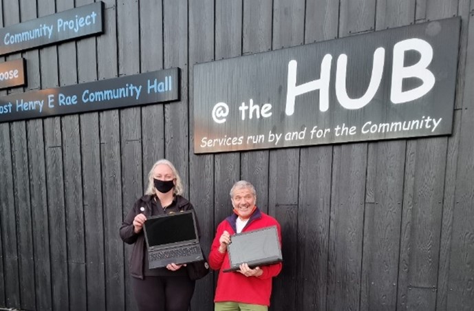 Photograph of two Farrans staff members holding donated laptops outside the hub