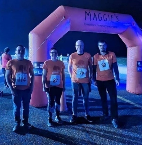 Photograph of 4 Jacobs employees standing infront of the start line of the 'Run the Runway' event at night