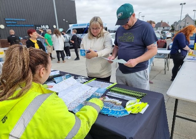 A photograph of a Farrans employee sitting at stand with promotional information at Active Travel day with 2 members of public at stand reading information