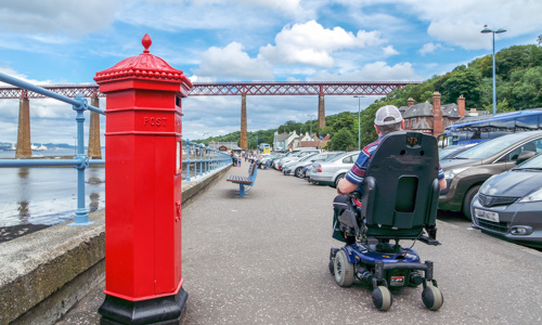 Person wheeling past a red post box on a pavement near the Forth Rail Bridge