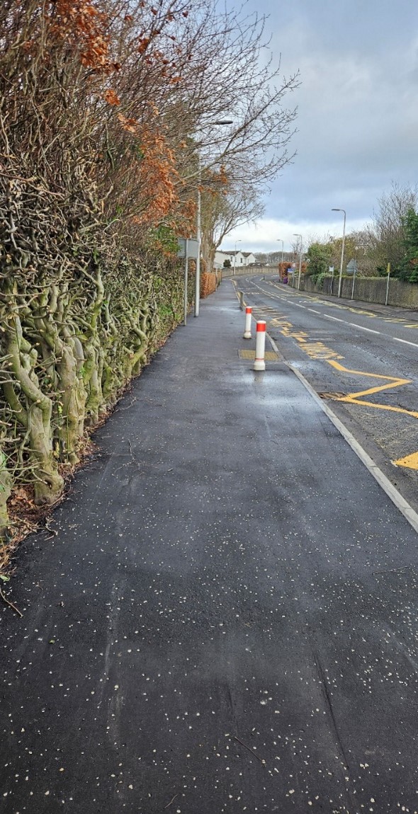 A resurfaced footway with safety bollards along the edge to prevent vehicles parking on the pavement. The road has new yellow no-parking lines.