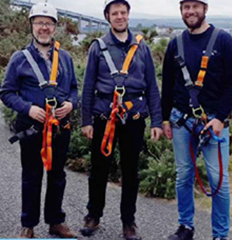 Three people standing and wearing zipline gear