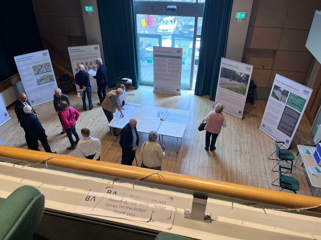 View looking down on the community engagement event space, showing people in the hall viewing banners and talking with the project team.