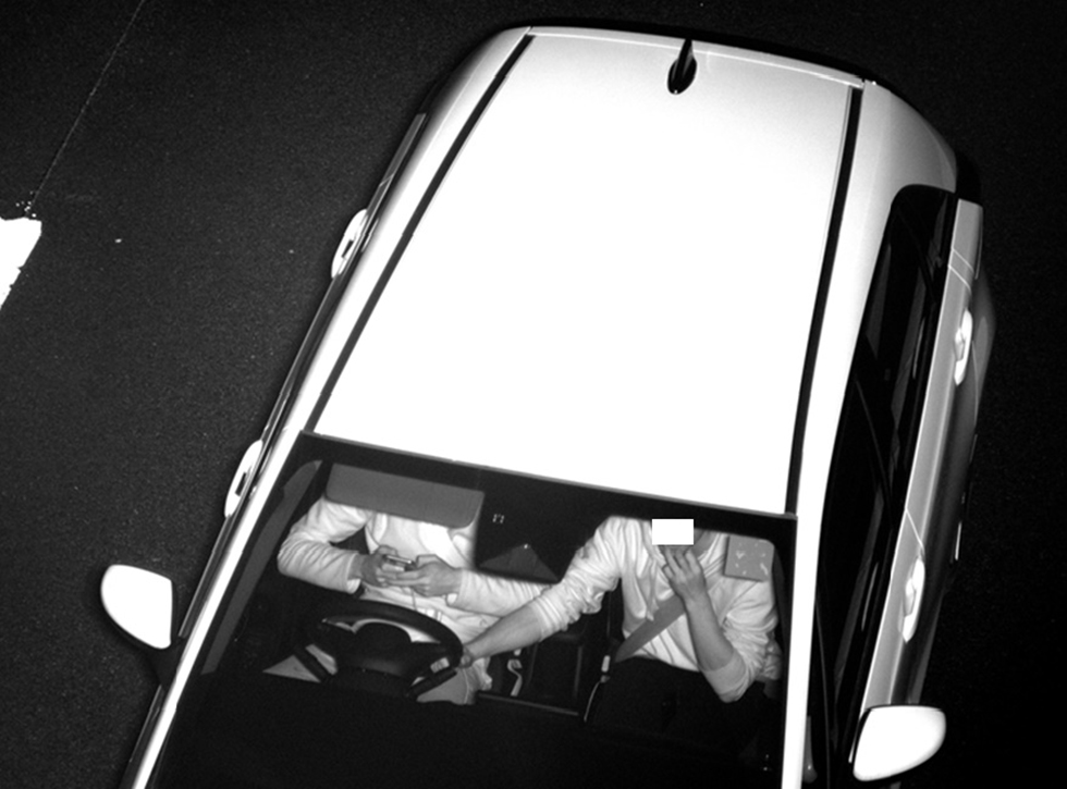 A driver uses a mobile phone, while the passenger holds the steering wheel